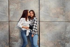 com xícara de café. lindas amigas alegres ou casal de lésbicas juntos perto da parede ao ar livre durante o dia foto