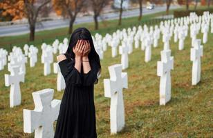 jovem mulher em roupas pretas, visitando o cemitério com muitas cruzes brancas. concepção de funeral e morte foto