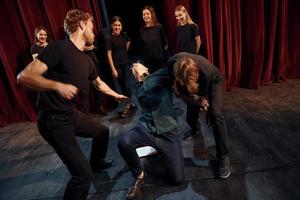 cena de luta. grupo de atores em roupas de cor escura no ensaio no teatro foto