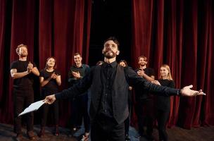 cara expressional praticando seu papel. grupo de atores em roupas de cor escura no ensaio no teatro foto