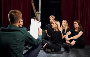 sentado no chão. grupo de atores em roupas de cor escura no ensaio no teatro foto