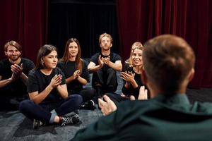 sentado no chão. grupo de atores em roupas de cor escura no ensaio no teatro foto