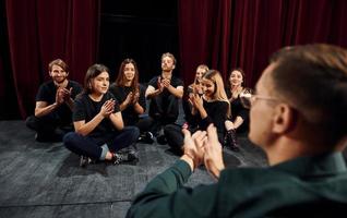 sentado no chão. grupo de atores em roupas de cor escura no ensaio no teatro foto