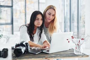 com laptop e câmera. duas jovens freelancers trabalhando dentro de casa no escritório durante o dia foto