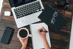 vista do topo. jovem freelancer trabalhando dentro de casa no escritório durante o dia. notebook e bloco de notas foto