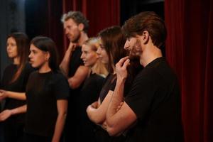 vista lateral. grupo de atores em roupas de cor escura no ensaio no teatro foto