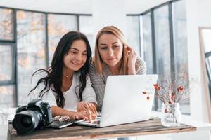 com laptop e câmera. duas jovens freelancers trabalhando dentro de casa no escritório durante o dia foto