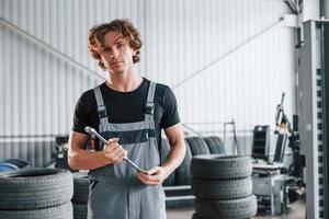 mantém a chave na mão. homem adulto em uniforme de cor cinza trabalha no salão do automóvel foto