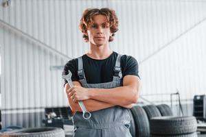 mantém a chave na mão. homem adulto em uniforme de cor cinza trabalha no salão do automóvel foto