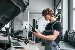 ferramenta especial para testar características. homem adulto em uniforme de cor cinza trabalha no salão do automóvel foto