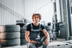 com ferramenta na mão. homem adulto em uniforme de cor cinza trabalha no salão do automóvel foto