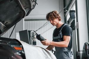 ferramenta especial para testar características. homem adulto em uniforme de cor cinza trabalha no salão do automóvel foto