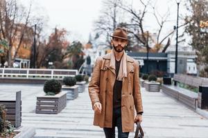 com saco. jovem modelo masculino em roupas da moda está ao ar livre na cidade durante o dia foto