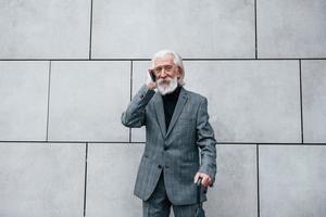 empresário sênior em roupas formais, com cabelos grisalhos e barba é falar ao ar livre por telefone foto