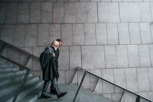 andando na escada. cara jovem com homem sênior em roupas elegantes está ao ar livre juntos. concepção de negócio foto