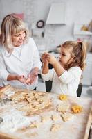 processo de ensino. avó sênior com sua neta cozinha doces para o natal na cozinha foto