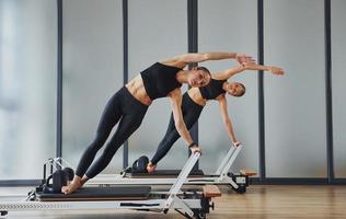 com auxílio de equipamentos de ginástica. duas mulheres em roupas esportivas e com corpos esguios têm um dia de ioga fitness dentro de casa juntas foto