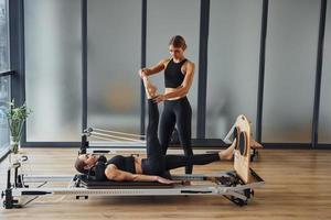 treinador ajudando garota. duas mulheres em roupas esportivas e com corpos esguios têm um dia de ioga fitness dentro de casa juntas foto