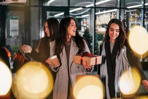 copos de bebida nas mãos. três mulheres alegres passam as férias de natal juntas ao ar livre. concepção de ano novo foto