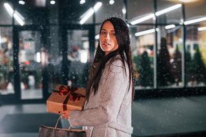 posa para a câmera e segura a caixa de presente. mulher alegre está ao ar livre na época das férias de natal. concepção de ano novo foto