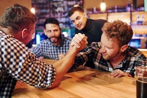 amigos joga queda de braço. grupo de pessoas juntas dentro de casa no pub se divertem no fim de semana foto