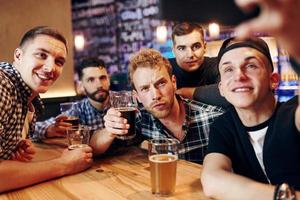 homem leva selfie por telefone. grupo de pessoas juntas dentro de casa no pub se divertem no fim de semana foto