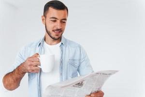 lê jornal. jovem bonito em pé dentro de casa contra um fundo branco foto