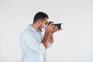 com câmera profissional. jovem bonito em pé dentro de casa contra um fundo branco foto