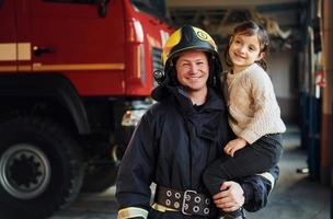 menina feliz está com bombeiro masculino em uniforme de proteção foto