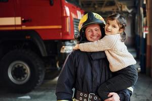 menina feliz está com bombeiro masculino em uniforme de proteção foto