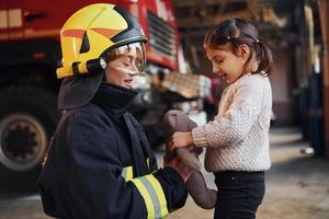 menina feliz está com bombeiro feminino em uniforme de proteção foto