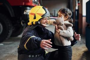 menina feliz está com bombeiro masculino em uniforme de proteção foto