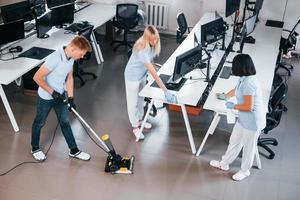 limpa chão. grupo de trabalhadores limpa escritório moderno juntos durante o dia foto