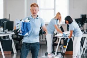 homem segura cesta. grupo de trabalhadores limpa escritório moderno juntos durante o dia foto