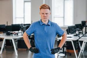 retrato de jovem de camisa azul e luvas pretas de proteção. de pé no escritório foto