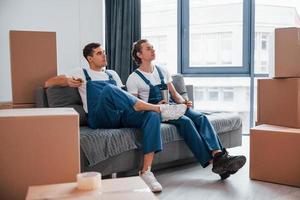 sentado no sofá. cansado e descansando. dois jovens em uniforme azul trabalhando dentro de casa na sala foto