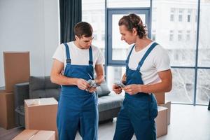 segurando dinheiro. dois jovens em uniforme azul trabalhando dentro de casa na sala foto