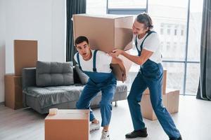 caixas pesadas. dois jovens em uniforme azul trabalhando dentro de casa na sala foto