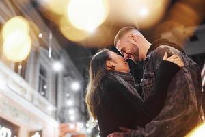 abraçando um ao outro. feliz casal multirracial juntos ao ar livre na cidade comemorando o ano novo foto