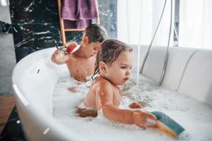 duas crianças se divertindo e se lavando no banho em casa. ajudando uns aos outros foto