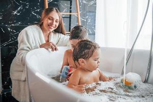 jovem mãe ajuda seu filho e filha. duas crianças lavando no banho foto