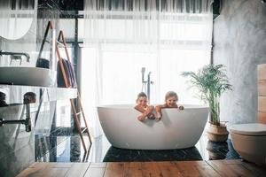 duas crianças se divertindo e se lavando no banho em casa. posando para uma câmera foto