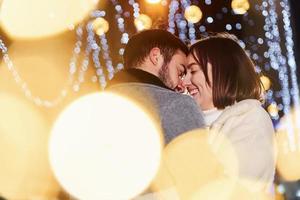 bela guirlanda de iluminação. casal jovem feliz comemorando o ano novo ao ar livre na rua foto