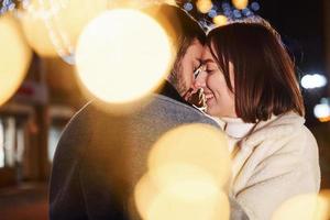 bela guirlanda de iluminação. casal jovem feliz comemorando o ano novo ao ar livre na rua foto