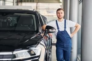 vista frontal do carro. jovem de camisa branca e uniforme azul conserta automóvel foto