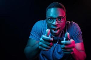 joga o jogo usando o controlador. iluminação neon futurista. jovem afro-americano no estúdio foto