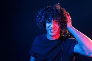 jovem dj com cabelo encaracolado em pé no clube com luz neon foto