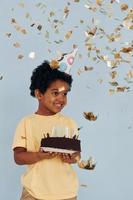 criança afro-americana feliz se diverte dentro de casa na festa de aniversário segura bolo foto
