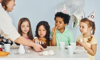 mulher segura bolo. as crianças comemorando a festa de aniversário dentro de casa se divertem juntas foto
