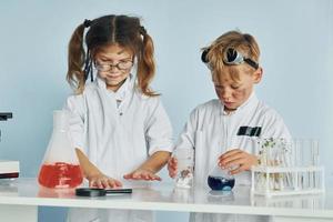 menina e menino em casacos brancos interpretam cientistas em laboratório usando equipamentos foto